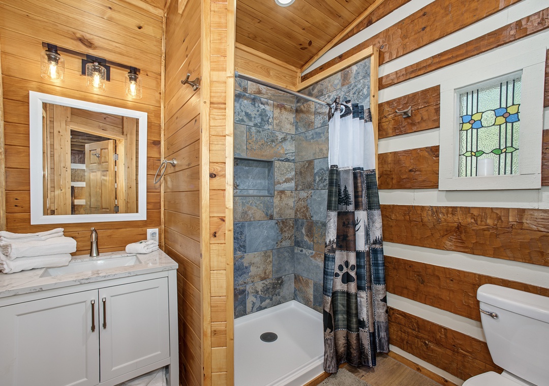 Your private bathroom blends rustic warmth with modern comfort—a bright vanity, stylish stone-tiled shower, and charming wood-paneled walls welcome you after a day of adventure.