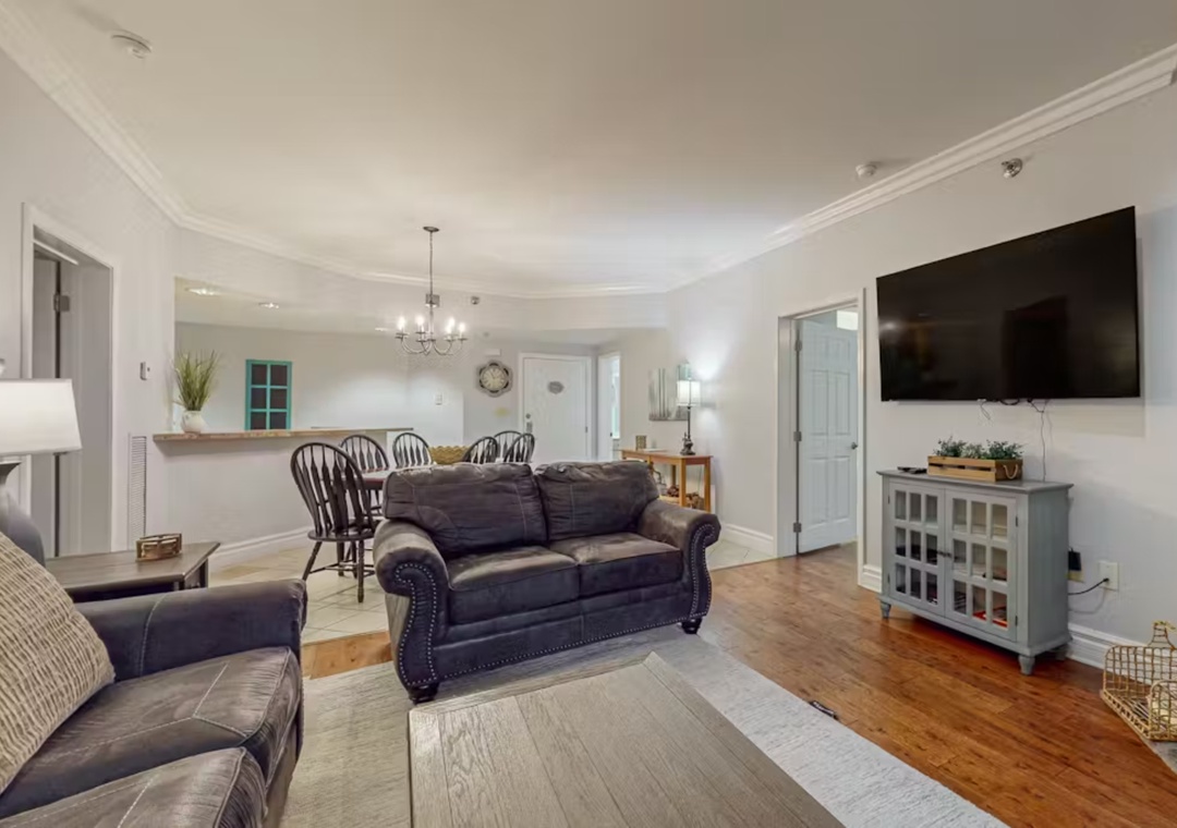 Relax in your spacious living room featuring plush leather seating, beautiful hardwood floors, and modern TV entertainment.