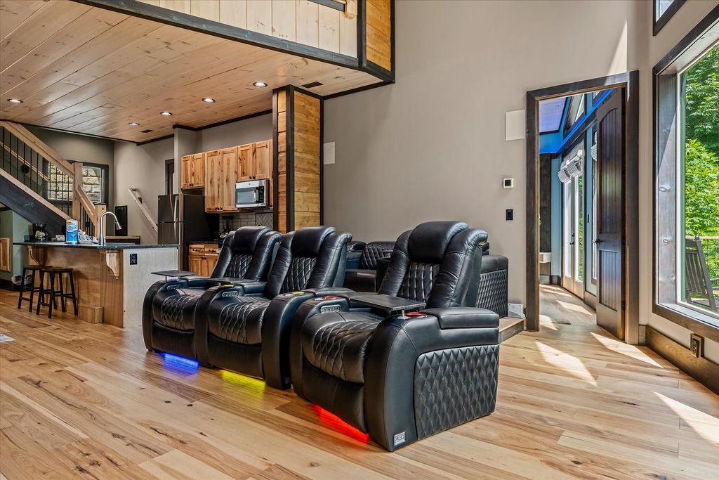 Sink into plush theater-style recliners with LED accent lighting in this stunning open-concept living space, where soaring ceilings and sunlit windows create the perfect retreat for movie nights.