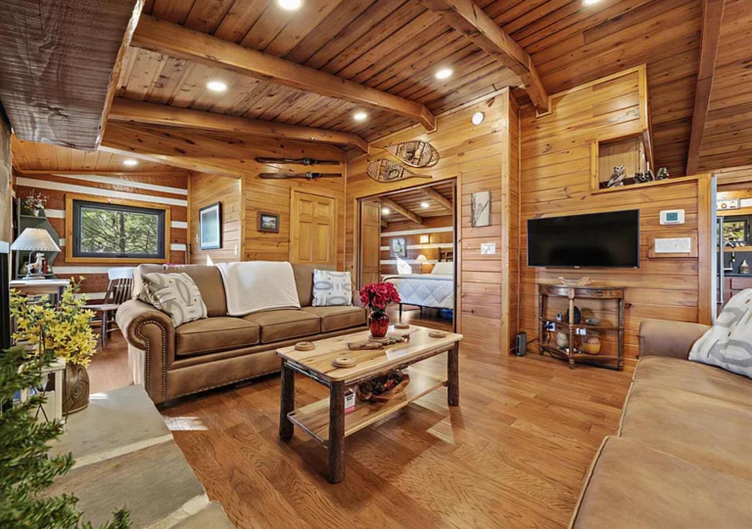 Sink into plush seating surrounded by warm wood walls and exposed beams. Your cozy retreat features modern entertainment, rustic charm, and a glimpse of the bedroom beyond—perfect for unwinding after mountain adventures.