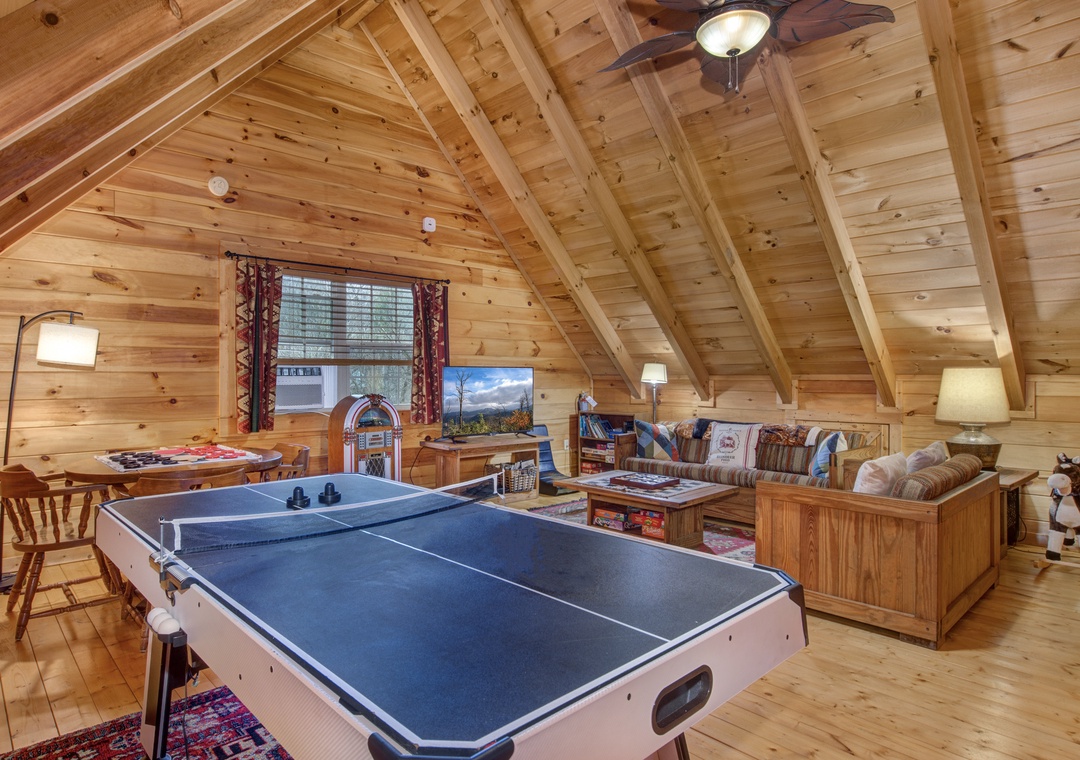 Your cozy loft game room invites hours of fun with ping pong, classic arcade games, and rustic charm under exposed wooden beams.