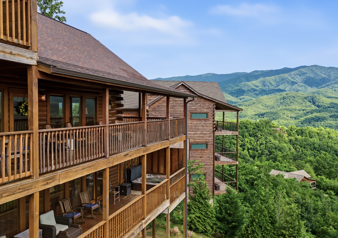 Mountain retreat featuring multi-level wooden balconies set against lush forested slopes and distant peaks under summer skies.