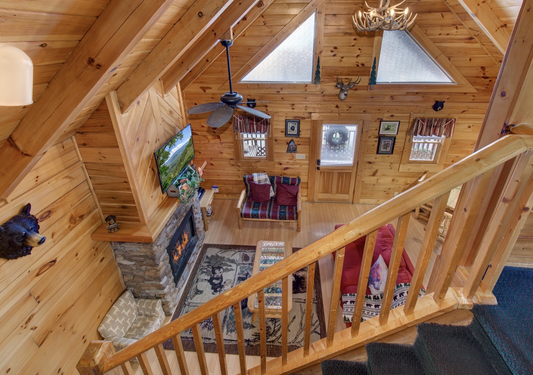 From the loft, you'll overlook your cozy cabin retreat with warm wood beams, stone fireplace, and comfortable seating.