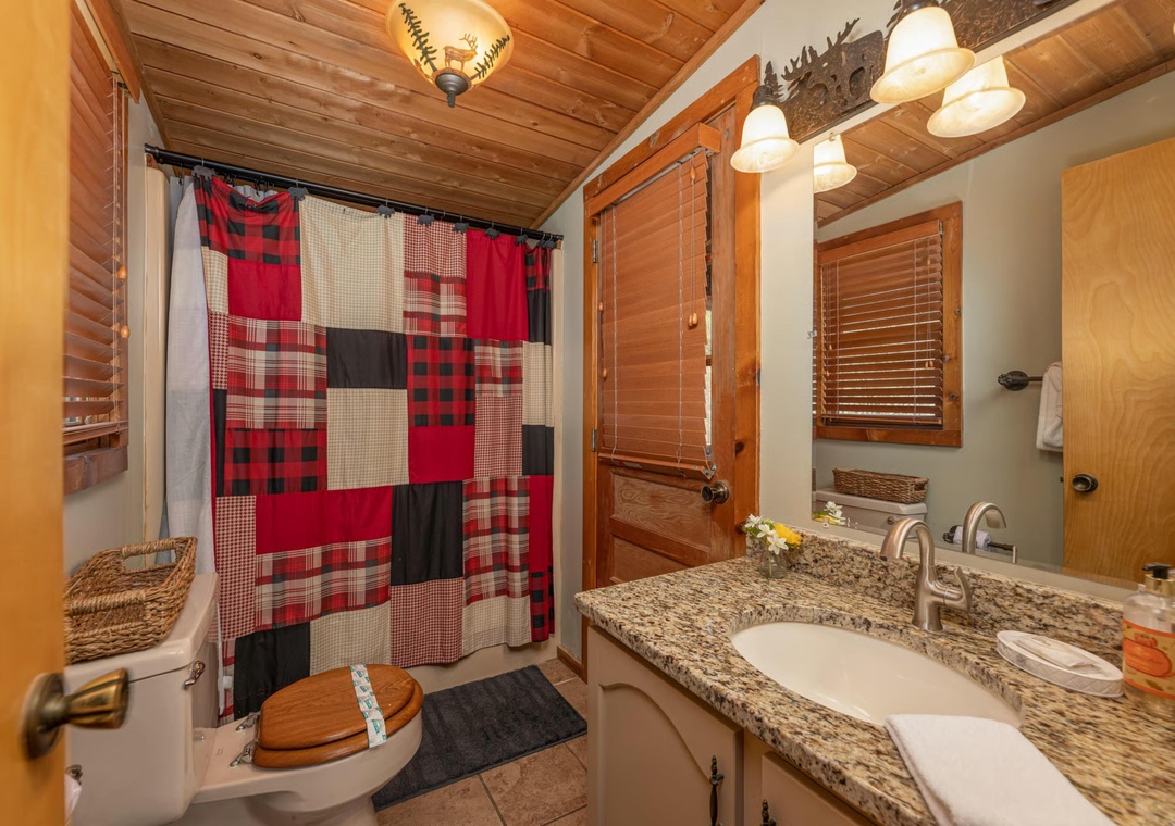 Your cozy bathroom features warm wood accents, a charming plaid shower curtain, and granite countertops—everything you need to unwind after a day of mountain adventures.