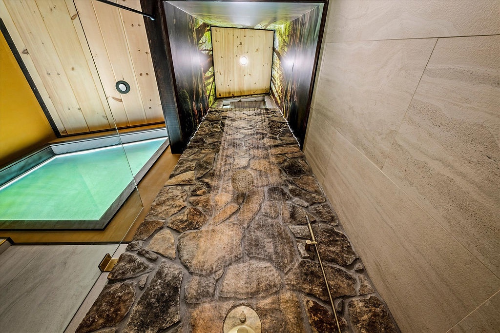A unique spa passage with dramatic stone flooring and backlit bamboo leads to your next relaxation experience, with a soothing hot tub waiting nearby.