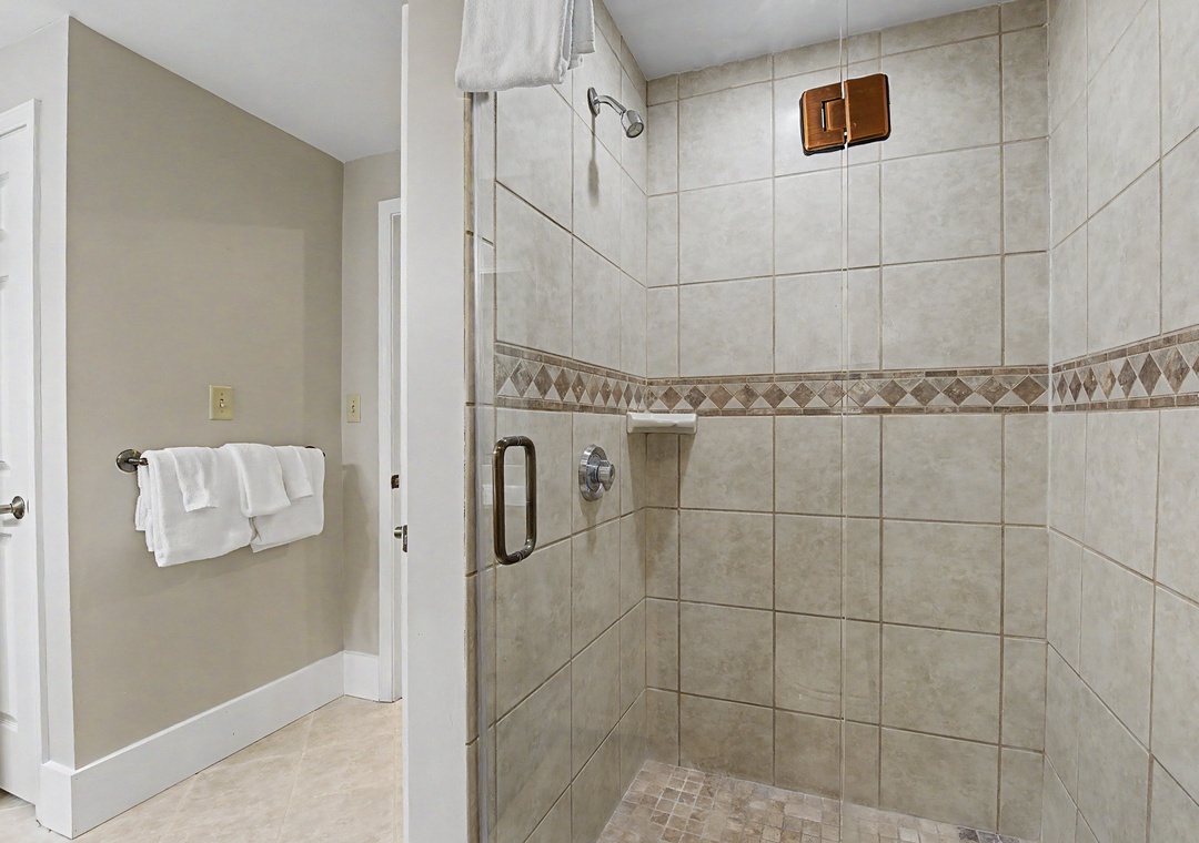 Step into your spacious walk-in shower with beautiful tile work and glass doors—fresh towels await nearby for your comfort.