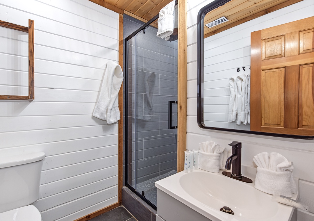 Step into your spa-like bathroom featuring a sleek modern shower, warm wood accents, and fresh linens ready for your arrival. The clean lines and bright shiplap create a serene retreat after your day.