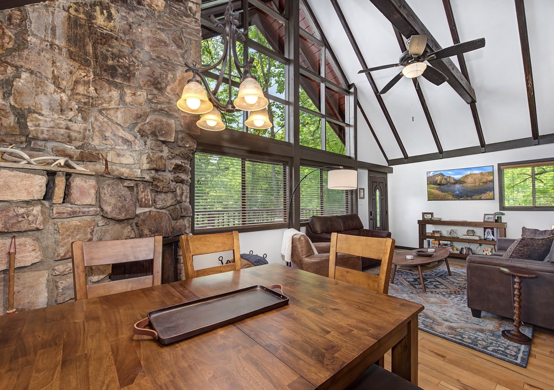 Sunlight streams through towering windows onto warm wood floors and a striking stone wall that anchors this open living space—your perfect retreat for relaxation and togetherness.