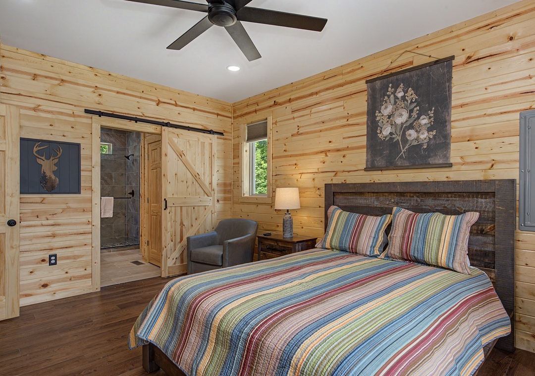 Drift off in your cozy cabin bedroom with rustic wood walls, a plush bed with vibrant linens, and a private ensuite bath with barn door charm.