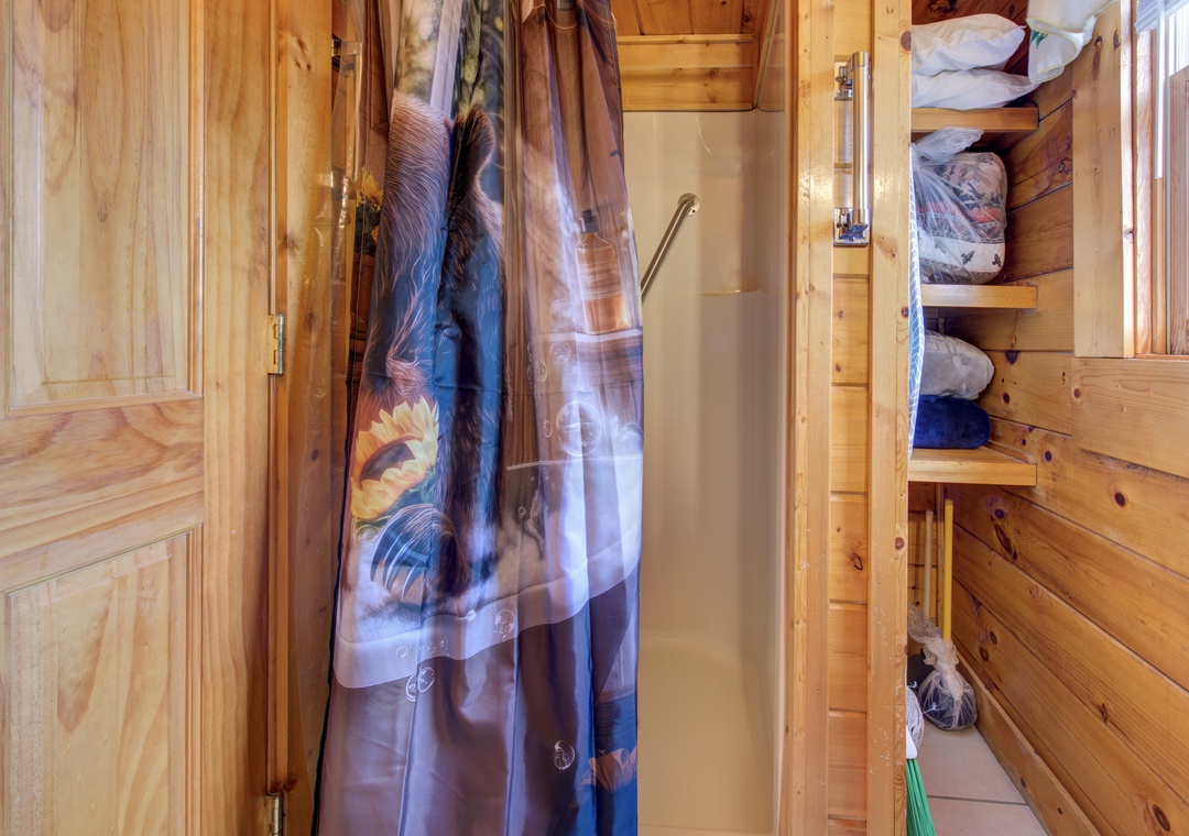 Your cozy wooden cabin bathroom features a refreshing shower with colorful curtains and clever bunk bed sleeping nooks nearby.