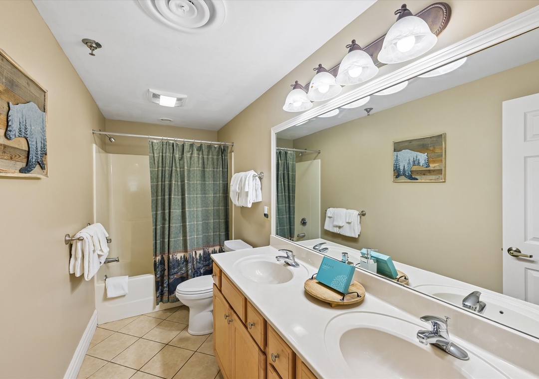 Your spacious bathroom features dual vanities, fresh towels, and a relaxing shower-tub combo with mountain-themed artwork creating a cozy retreat.