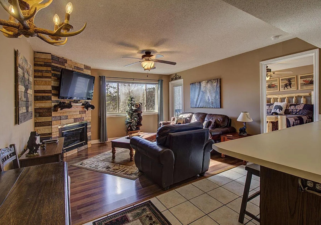 Relax in your cozy living room featuring a rustic stone fireplace, comfortable leather seating, and mountain lodge charm.