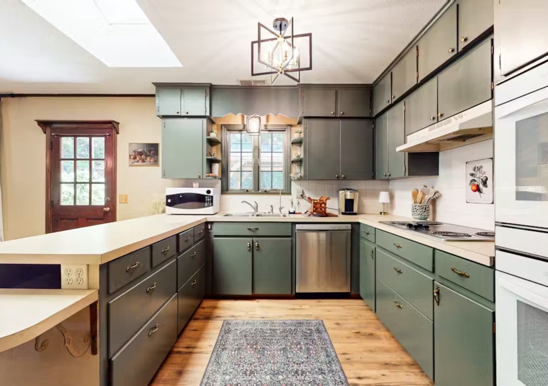Your spacious kitchen invites culinary adventures with sage-green cabinets, modern appliances, and warm wood floors that make cooking feel like home.
