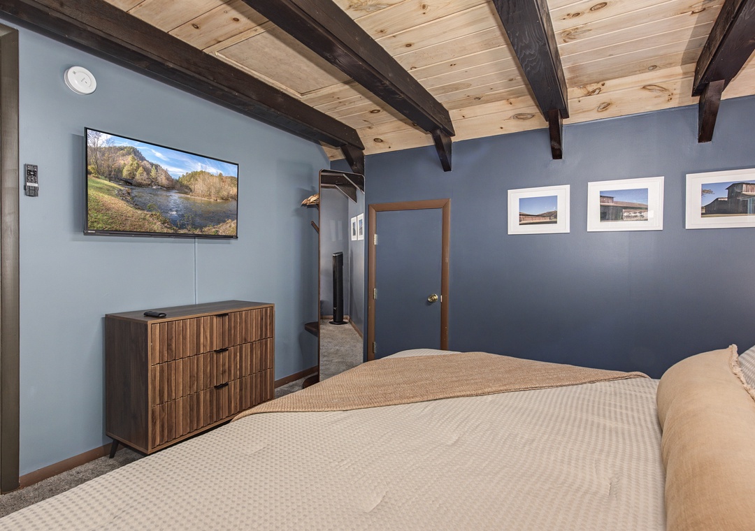 Unwind in your cozy bedroom featuring exposed wood beam ceilings, a wall-mounted TV for movie nights, and comfortable sleeping space designed for your complete relaxation.