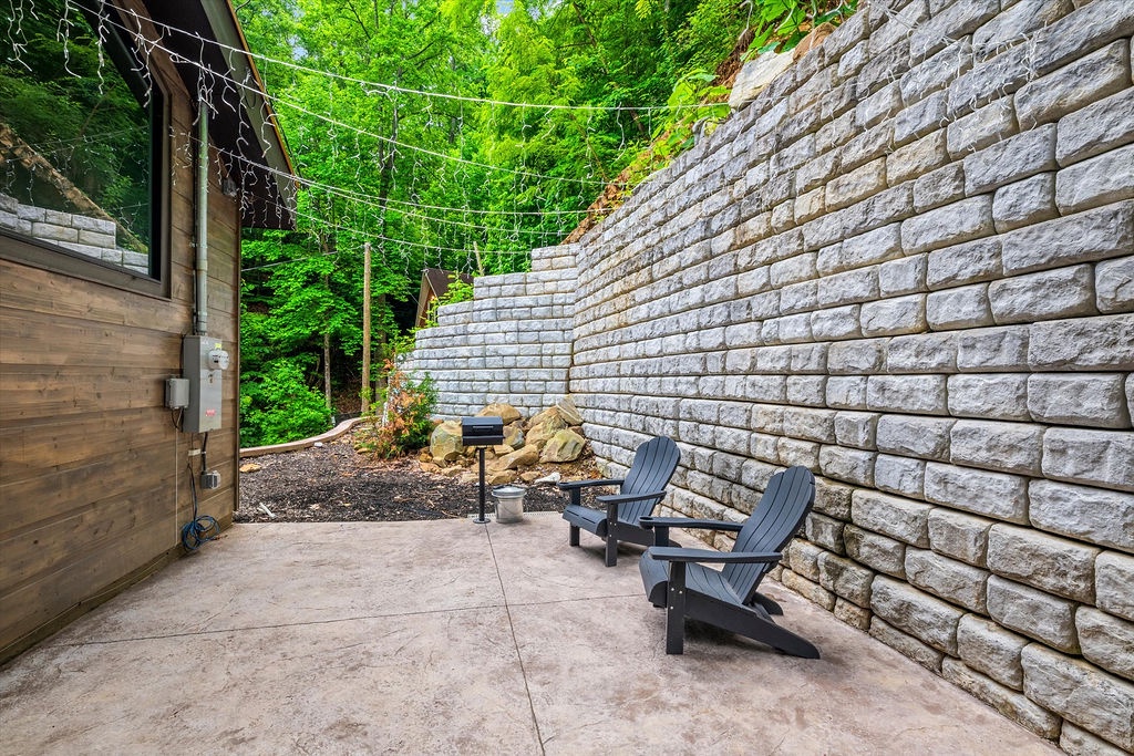 Settle into your private patio surrounded by nature and textured stone walls, where you can unwind in cozy Adirondack chairs under twinkling lights with forest views all around.