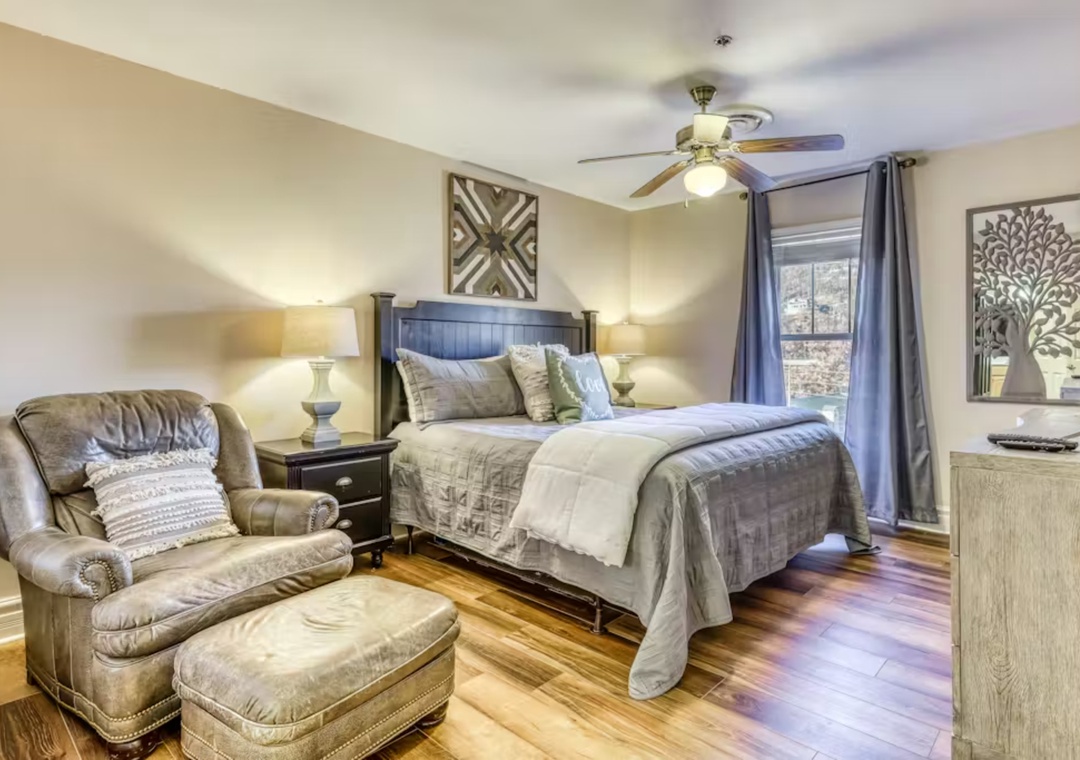 Relax in your spacious bedroom featuring a plush leather chair, elegant decor, and warm hardwood floors for ultimate comfort.