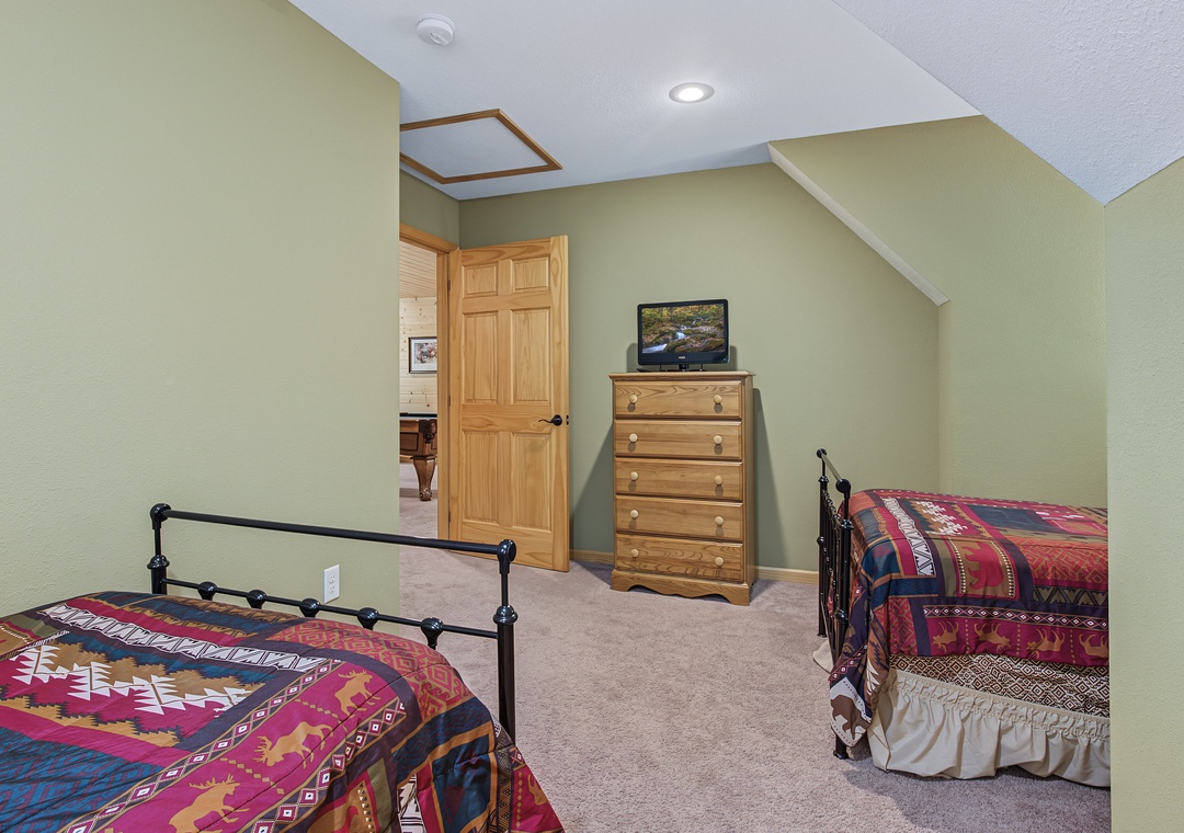 Unwind in your peaceful bedroom with twin beds dressed in vibrant quilts, vaulted ceilings, and thoughtful touches like a TV and wooden dresser for your comfort.