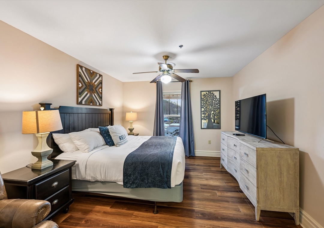 Relax in your serene bedroom featuring warm wood floors, ceiling fan, and modern touches for ultimate comfort.