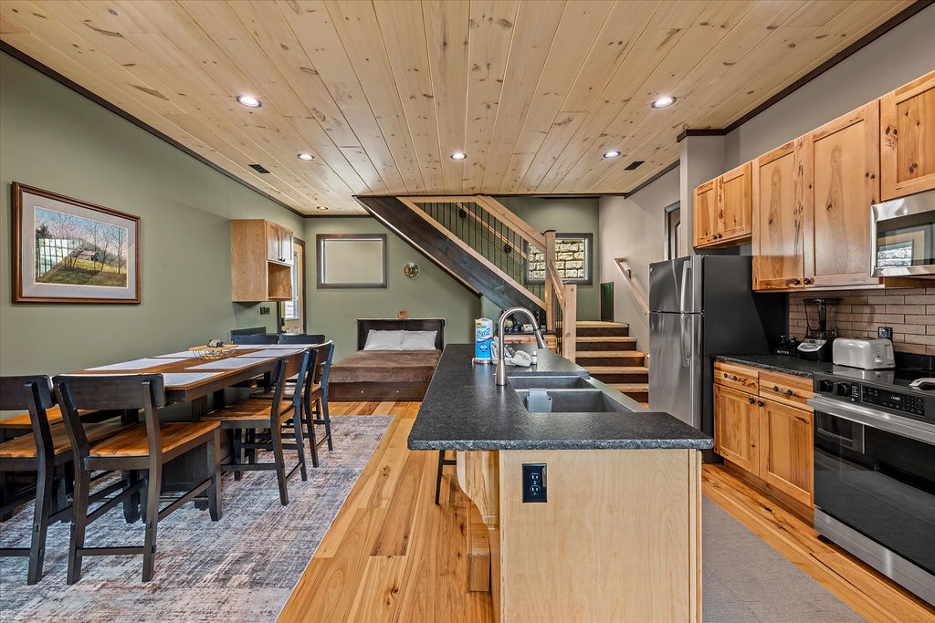 A bright, open living area with a well-equipped kitchen island, dining table, and rustic pine ceiling welcomes you to gather, cook, and unwind in comfortable style.