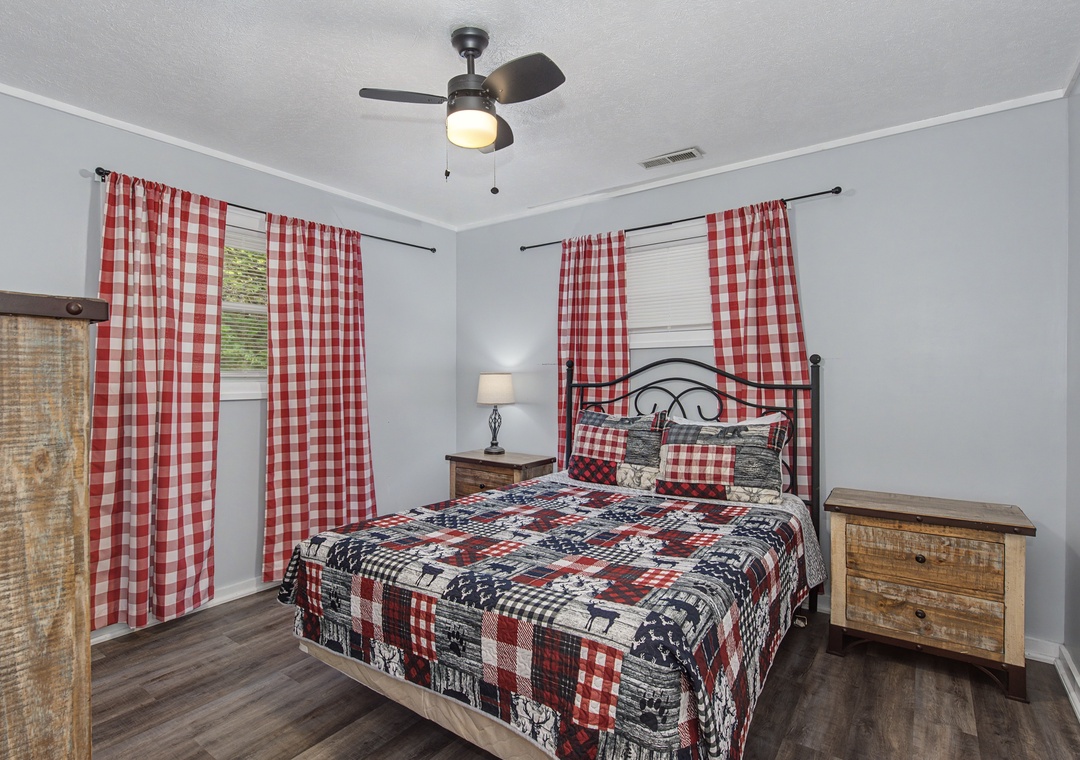 Cozy up in your charming bedroom featuring cheerful red checkered curtains, rustic wood furnishings, and a comfy quilted bed that promises sweet dreams.