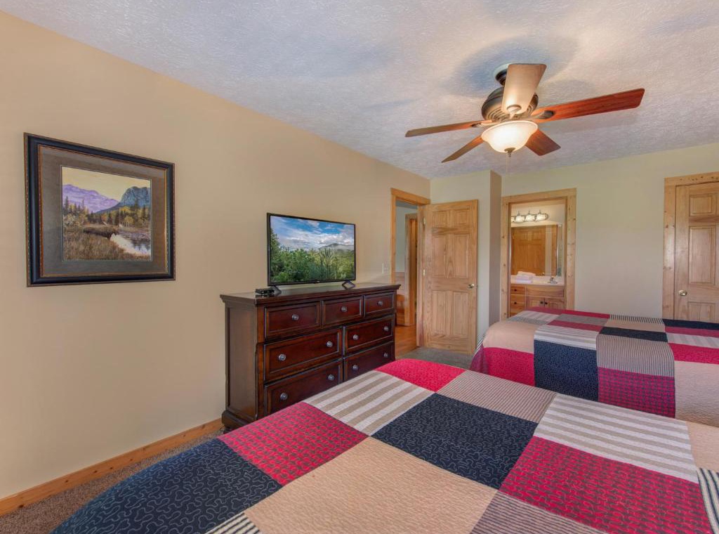 Drift off to sleep in your cozy bedroom, complete with twin beds, warm wood dresser, and gentle ceiling fan for perfect comfort.