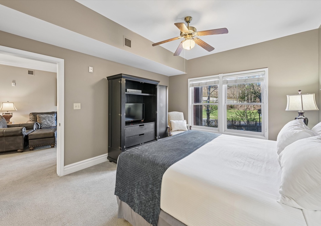 Your spacious master suite offers comfort with plush bedding, TV entertainment, and peaceful garden views through large windows.