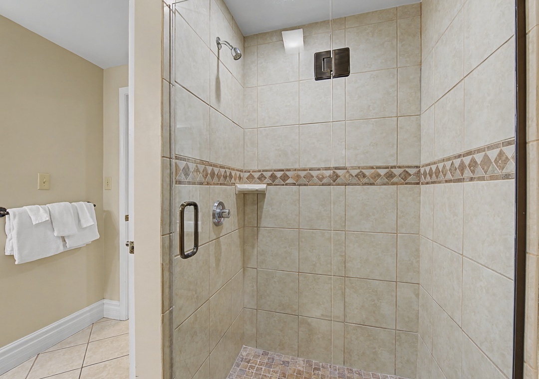 Step into your spacious tiled shower with decorative mosaic accents and glass doors, where fluffy white towels await your refreshing retreat.