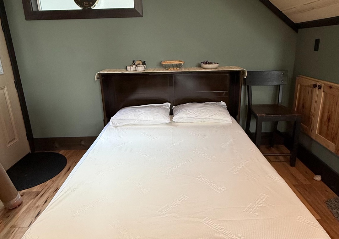 Retreat to your cozy bed with exposed beams, sage green walls, and a peaceful skylight view above your comfortable bed.