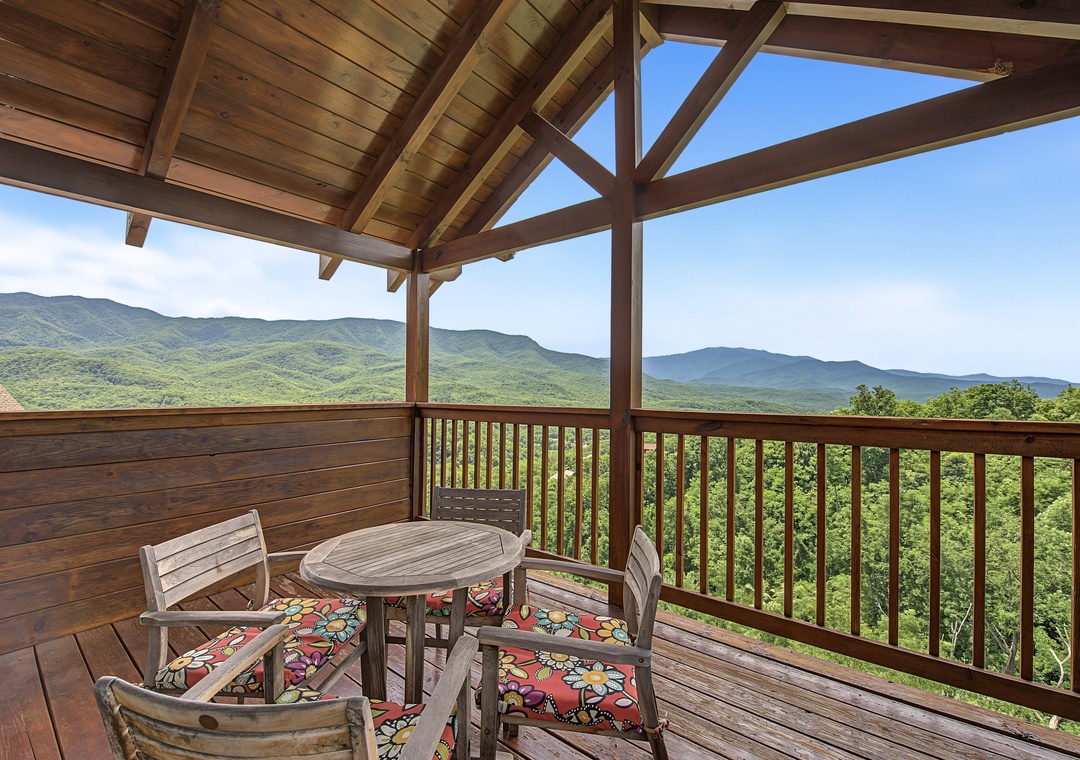 Picture yourself sipping morning coffee at this cozy table, gazing out at sweeping mountain views that stretch for miles. The covered deck keeps you comfortable while immersing you in nature's grandeur.