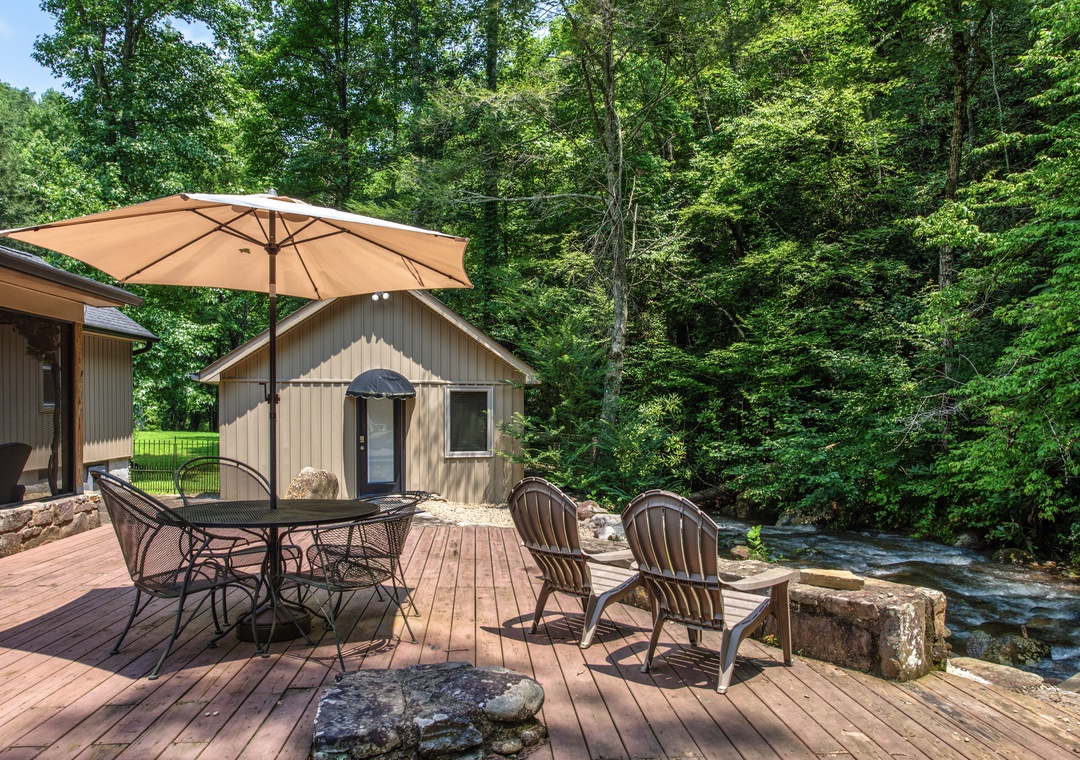 The property sits nestled in lush forest along a rushing stream, with spacious deck seating perfect for morning coffee or evening relaxation under the trees.