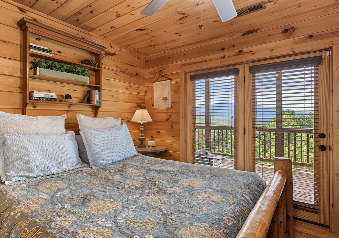 Wake up in this cozy cabin bedroom with expansive views through French doors, rustic wood paneling, and plush bedding that invites restful mountain getaways.