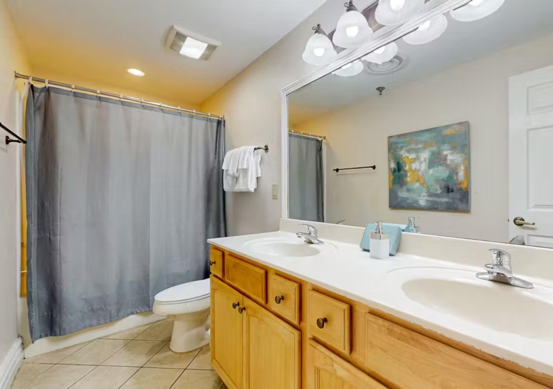 Refresh in your spacious dual-sink bathroom with warm wood cabinetry, overhead vanity lighting, and a relaxing tub-shower combo.