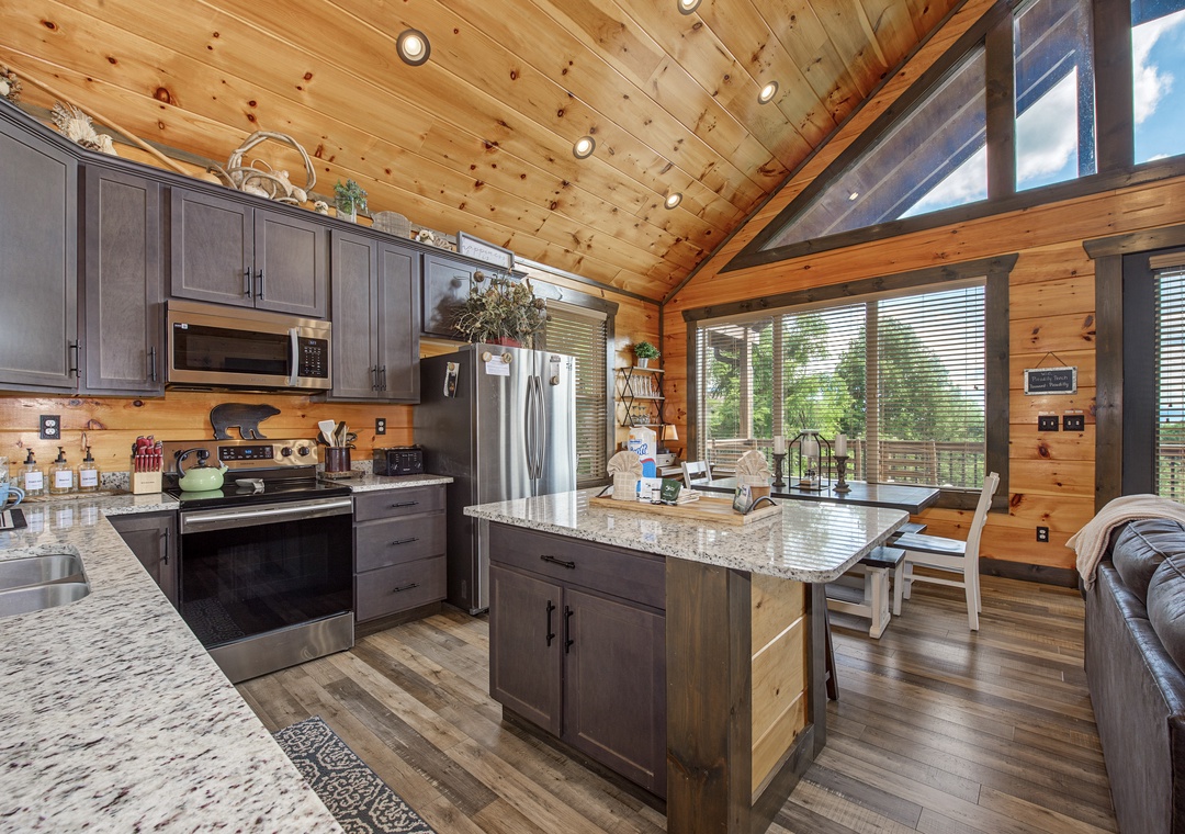 Your fully-equipped chef's kitchen features granite counters, stainless appliances, and a large island—all under soaring wood ceilings with natural light pouring in from expansive windows.