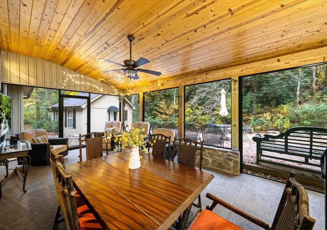 Gather around the warm wood dining table under soaring pine ceilings, where floor-to-ceiling windows frame lush forest views and sunlight streams onto your private screened porch retreat.