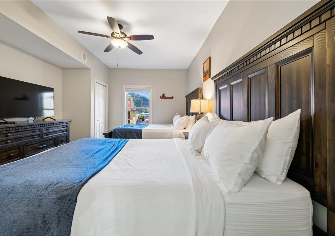Sink into luxury with two plush queen beds featuring crisp linens and blue accent throws. Your peaceful retreat includes a flat-screen TV and ceiling fan for optimal comfort.