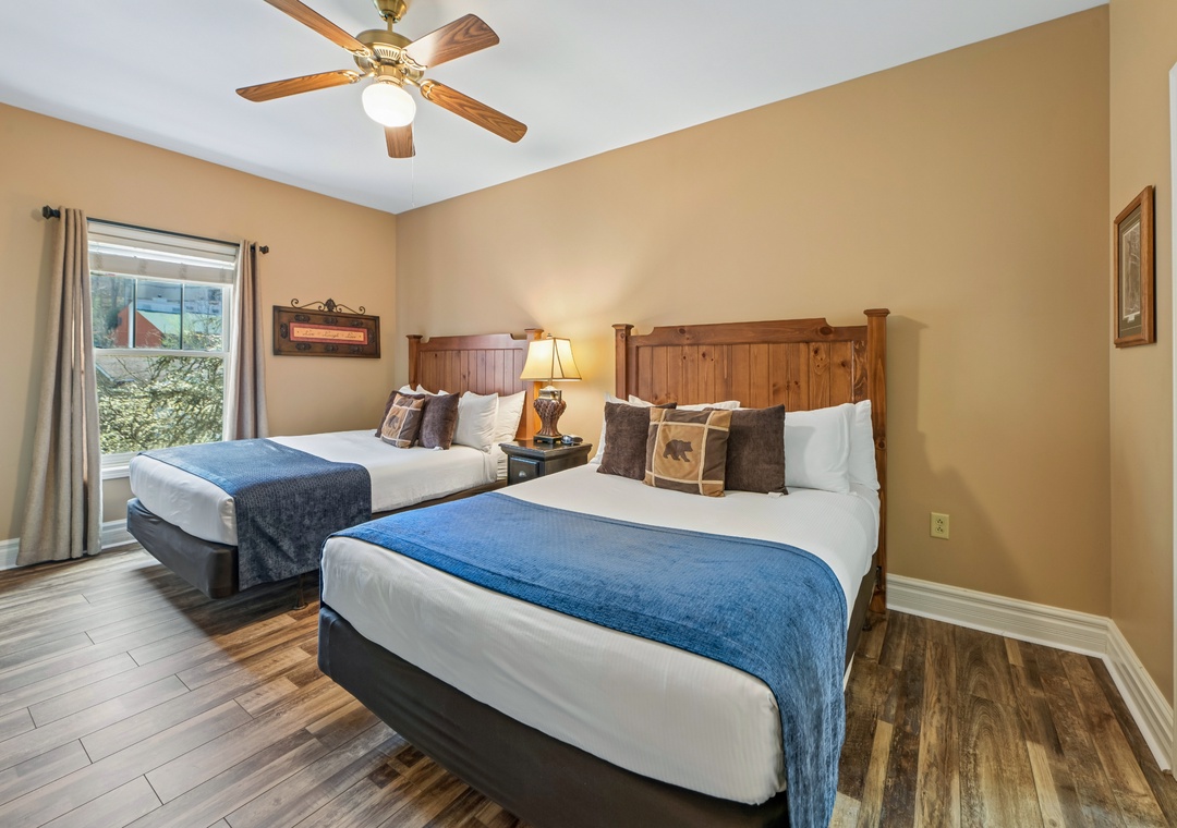 Your cozy mountain retreat features twin beds with rustic wood headboards and crisp linens beneath a gentle ceiling fan breeze.