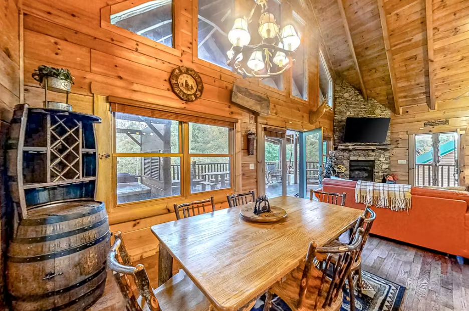Gather around this rustic dining table where warm wood surrounds you and sunlight streams through expansive windows, creating perfect moments for shared meals.