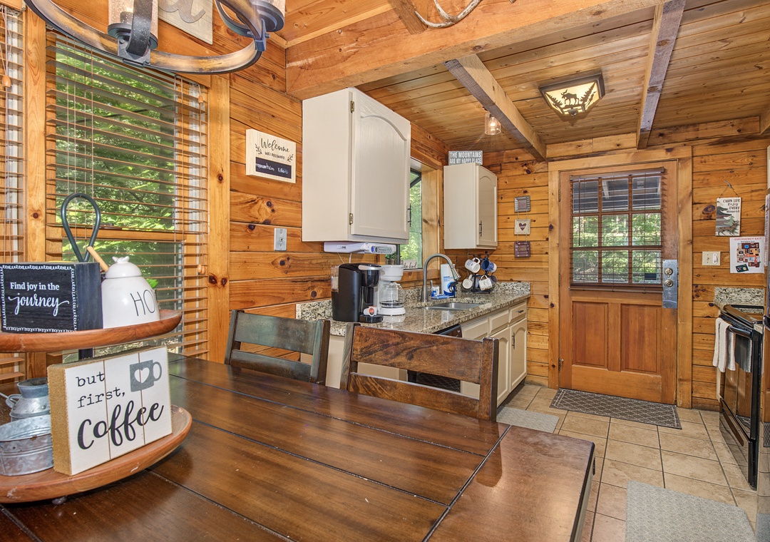 Start your mornings in this charming kitchen where rustic wood beams meet modern convenience. Your coffee station awaits, complete with everything you need to brew the perfect cup while gazing at greenery through warm wooden blinds.