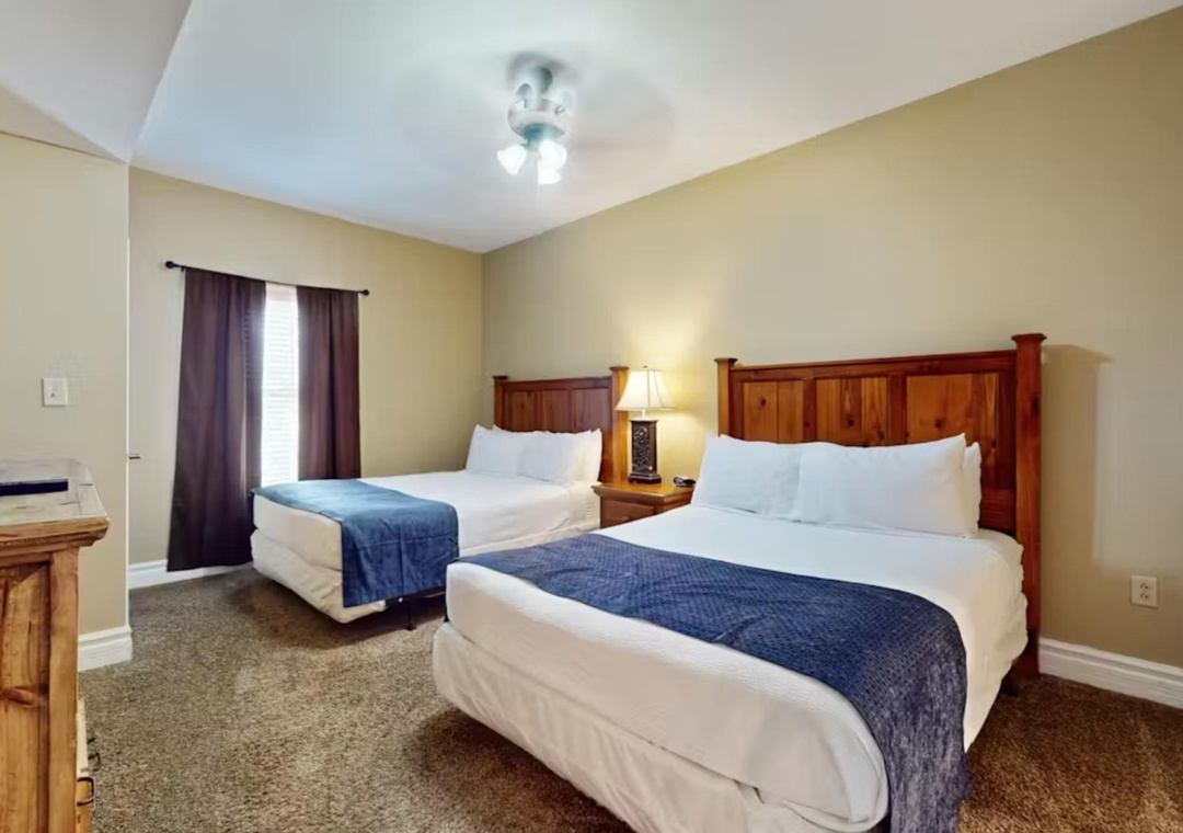 Rest comfortably in your spacious bedroom featuring two plush beds with crisp linens and warm wood furnishings for a peaceful night's sleep.