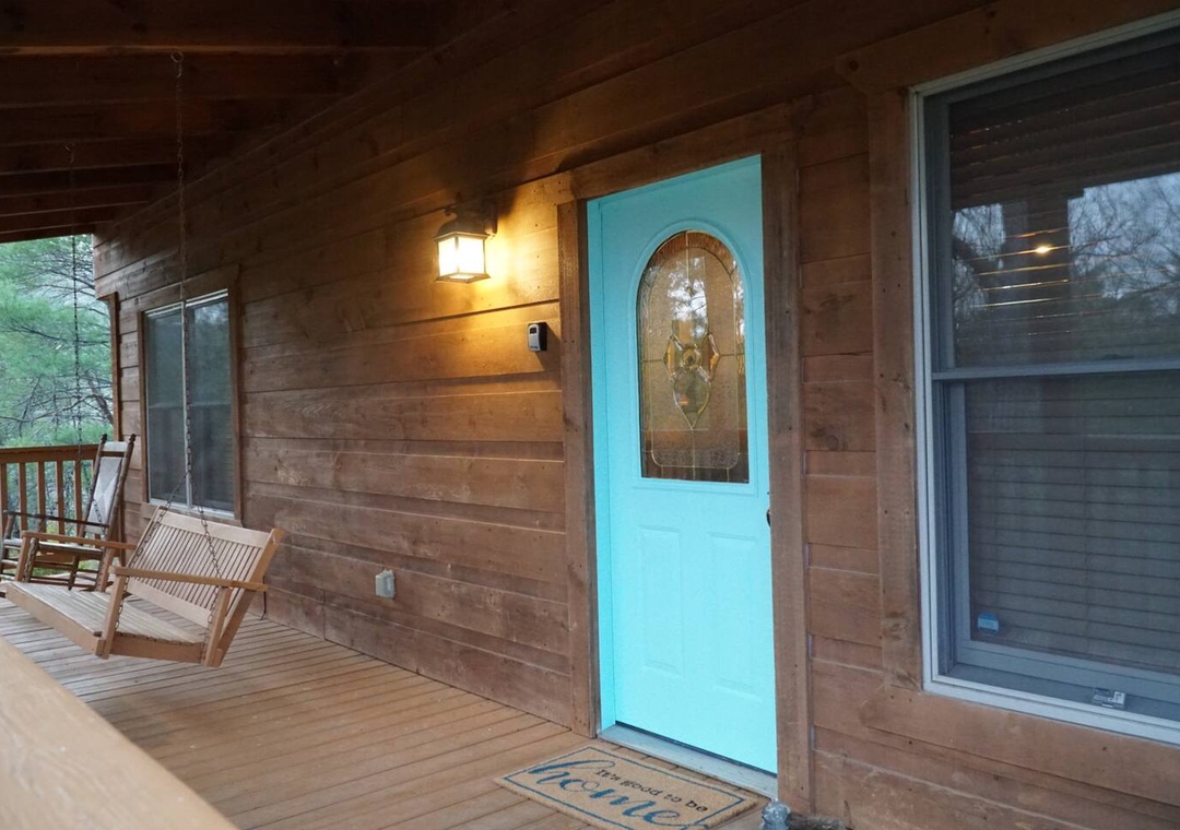 A charming turquoise door welcomes guests to this cozy log cabin, complete with a peaceful porch swing for relaxing evenings.