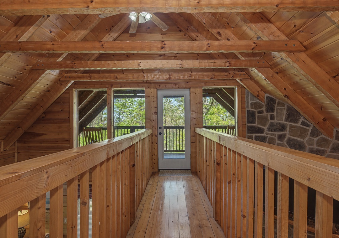 Step into your private loft sanctuary where rustic timber beams frame peaceful forest views through the balcony doors.