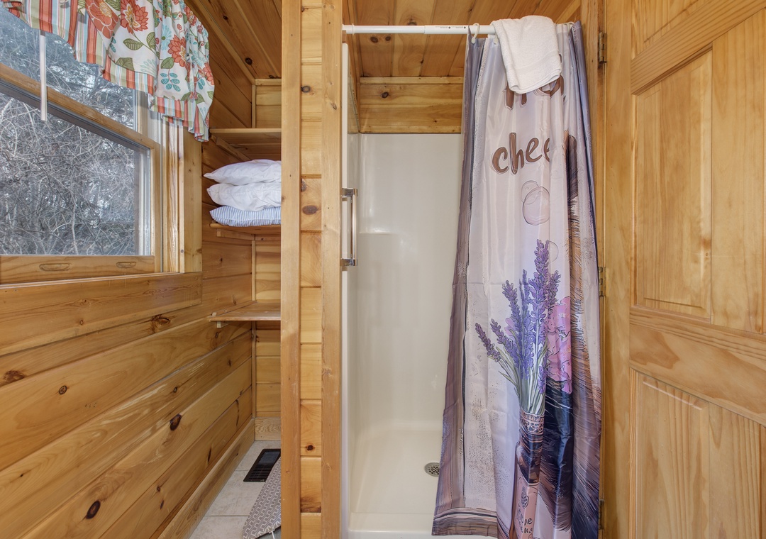 Cozy cabin bathroom with natural wood walls, charming lavender shower curtain, and thoughtful storage nooks for your comfort.
