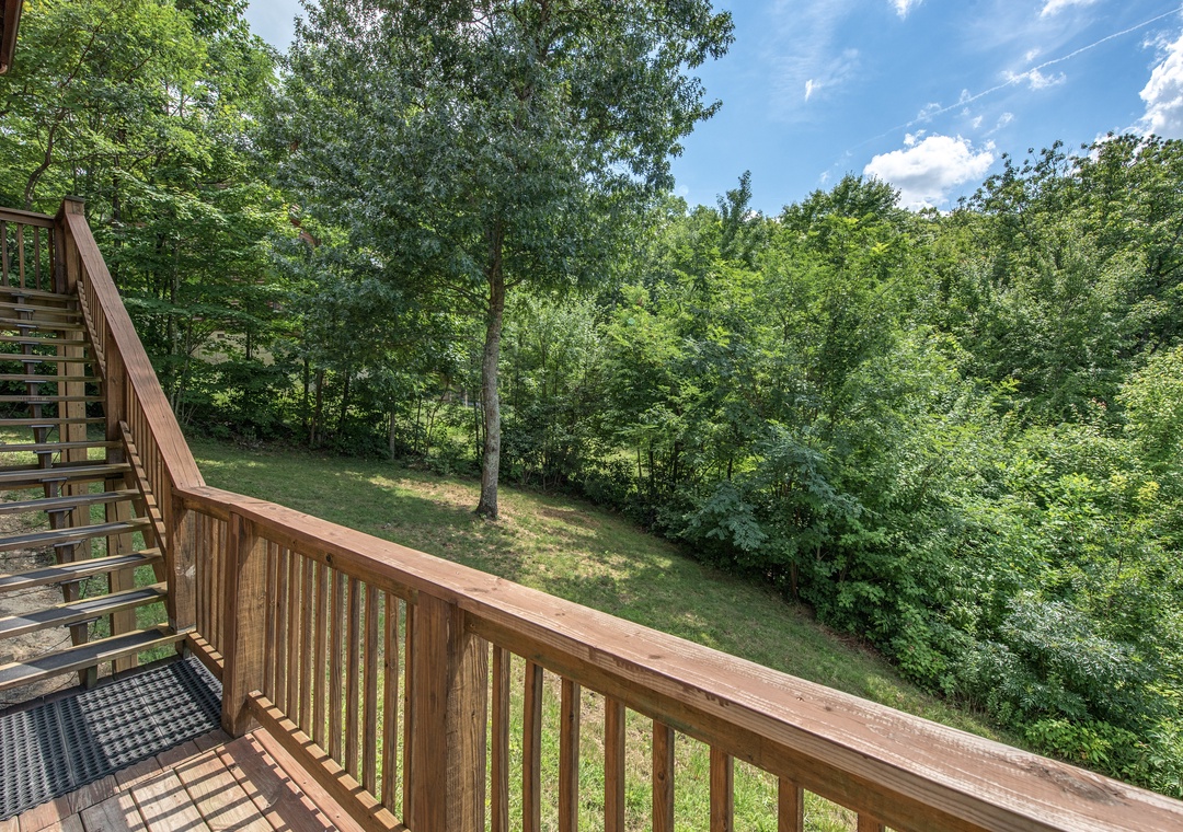 The property sits amid dense forest, offering peaceful natural surroundings. Exterior stairs lead to an elevated outdoor deck area above the treetops.