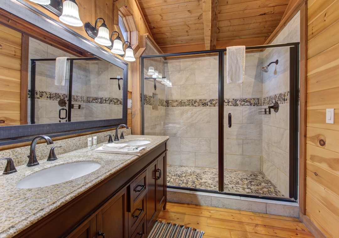 Unwind in your luxurious cabin bathroom featuring granite countertops, dual sinks, and a stunning walk-in shower with decorative stone accents.