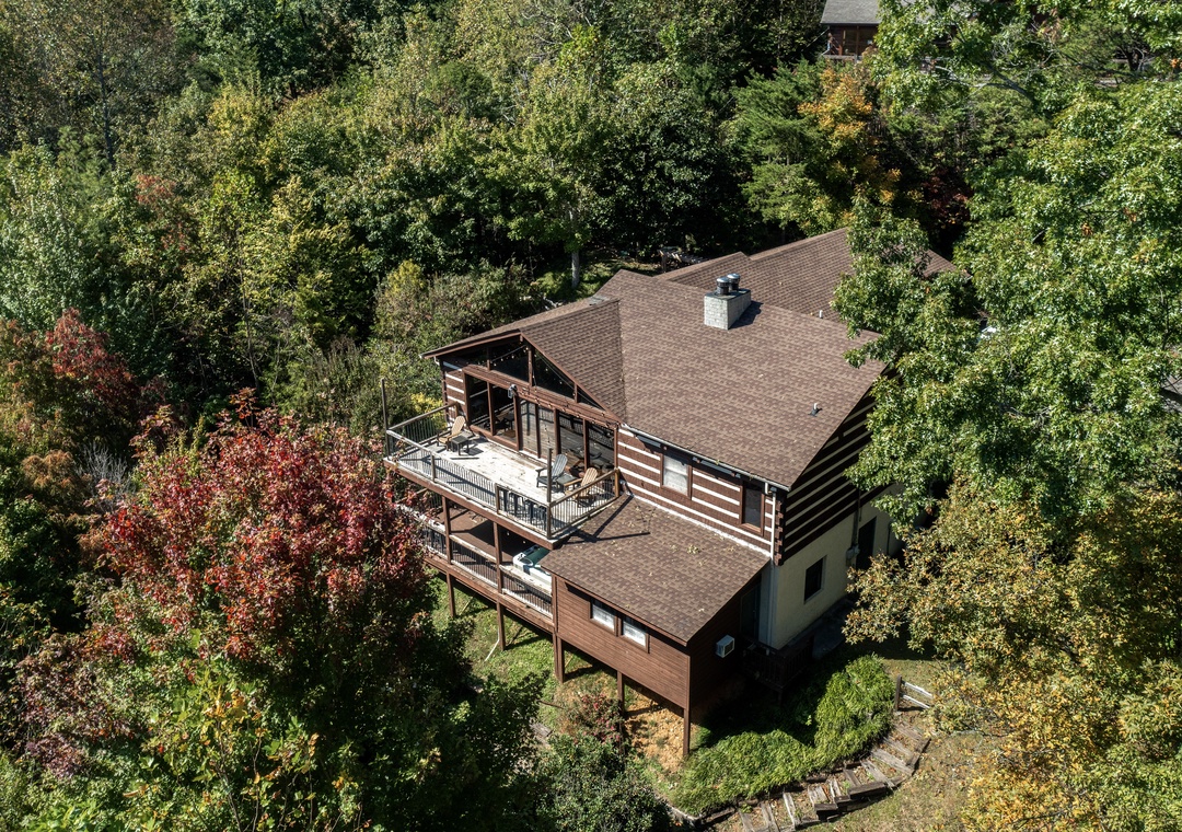An elevated mountain retreat nestled among vibrant autumn foliage, featuring rustic wood siding and expansive multi-level decks offering a peaceful wooded setting.