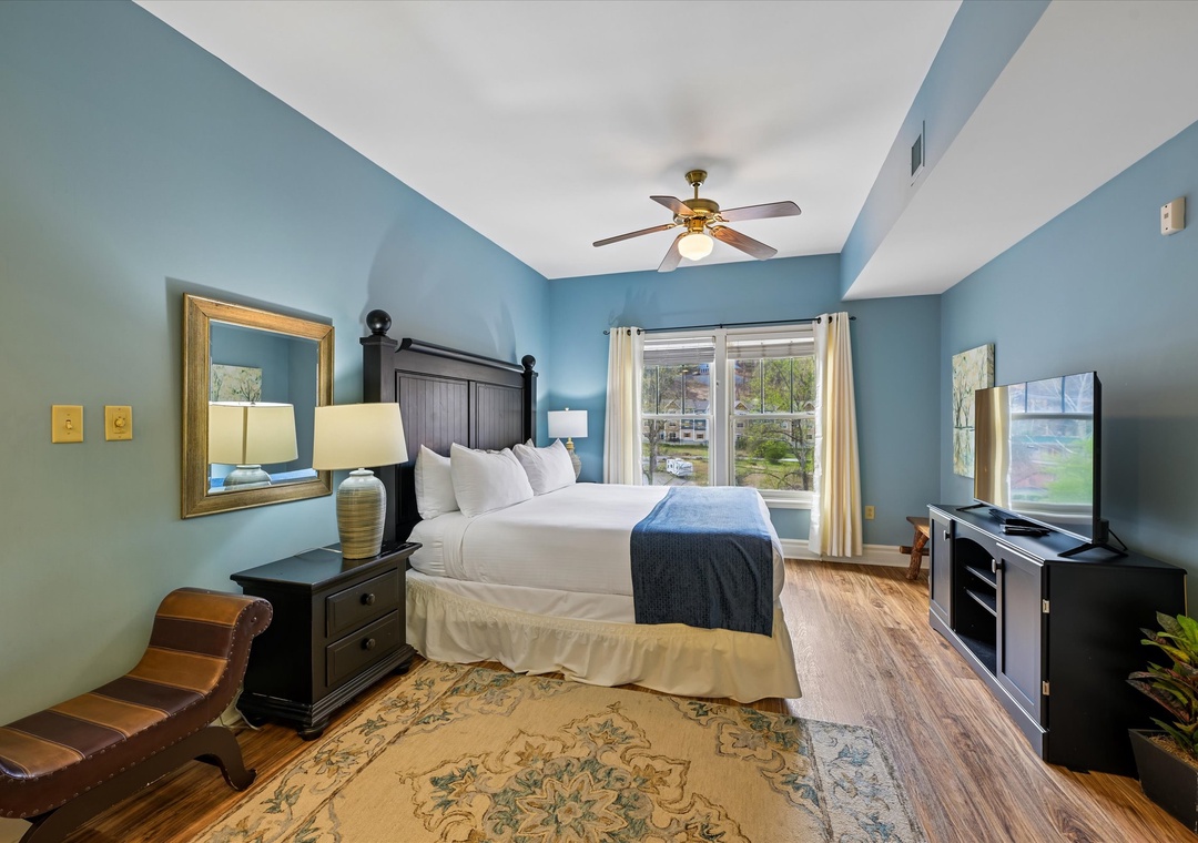 Unwind in your serene blue bedroom with plush bedding, warm wood floors, and peaceful views through large windows.