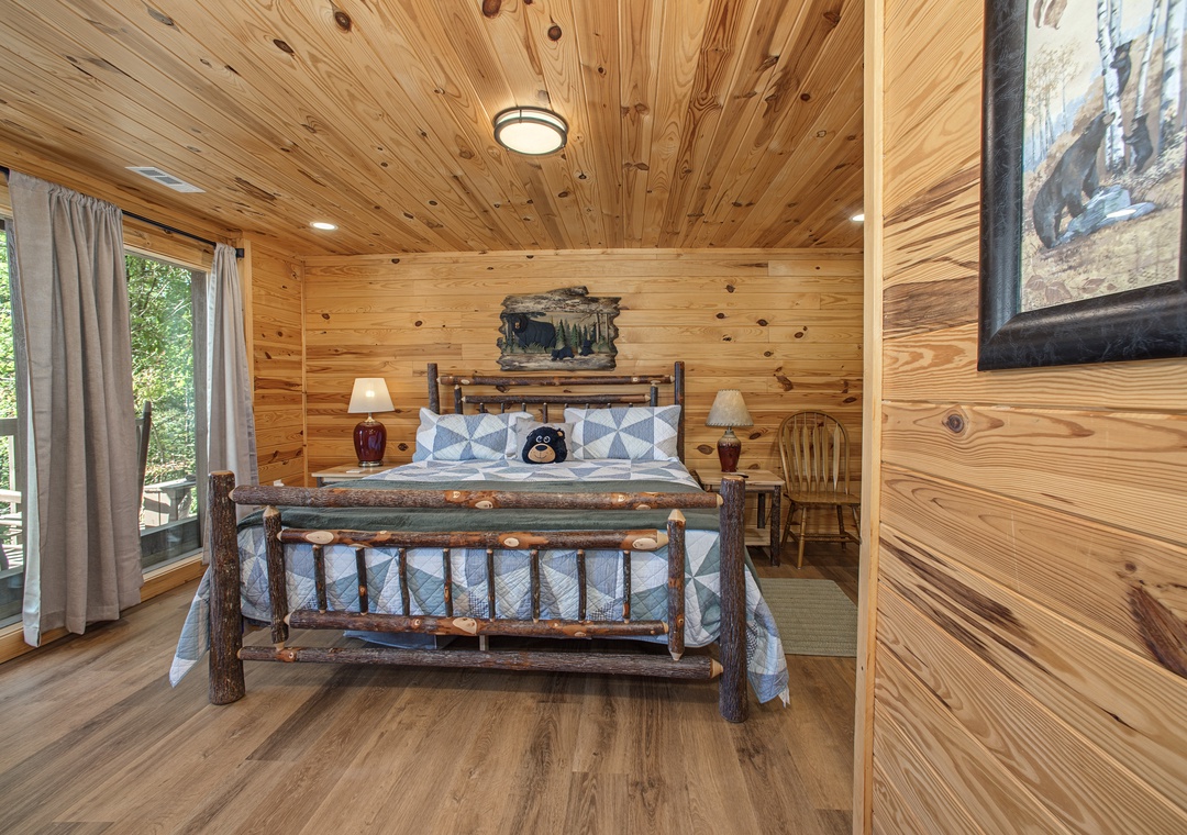 Unwind in your cozy cabin bedroom with rustic log-frame bed and warm knotty pine throughout, where peaceful forest views invite a restful night's sleep.
