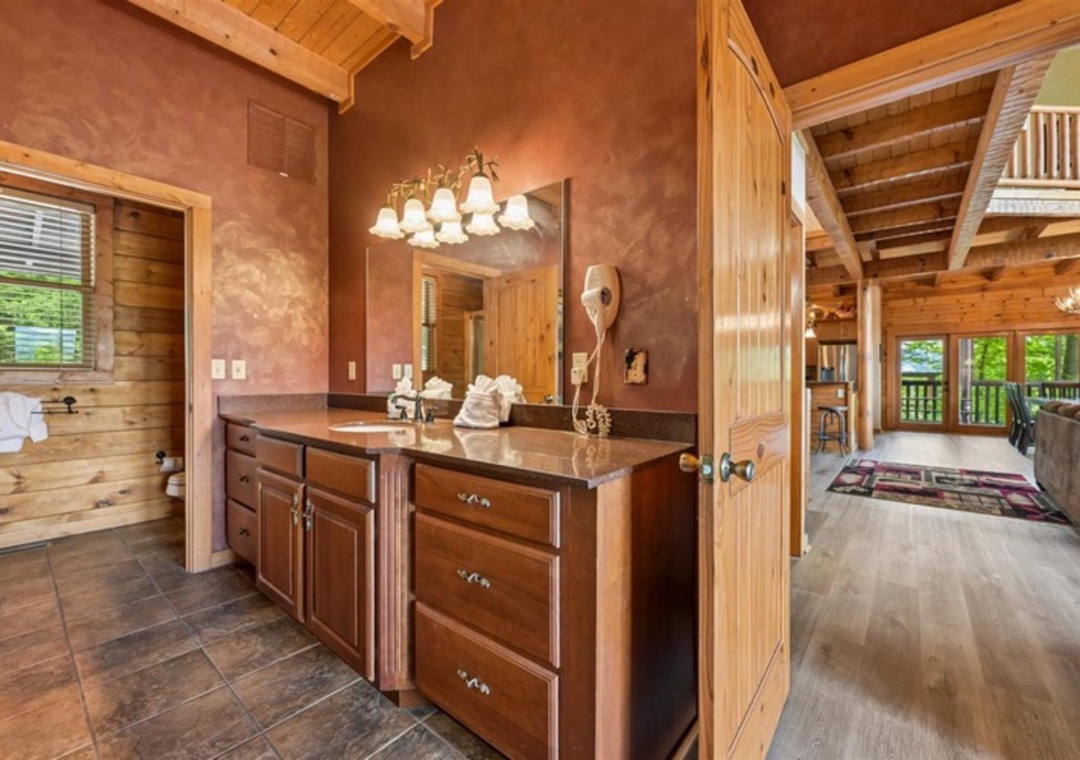 Your private bathroom features rustic charm with rich wood cabinetry, warm earth-toned walls, and exposed beam ceilings that create a cozy mountain retreat atmosphere.