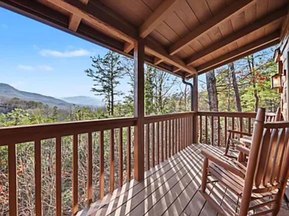 Covered deck offers sweeping mountain views through towering trees, with rocking chairs ready for relaxation in the fresh mountain air.