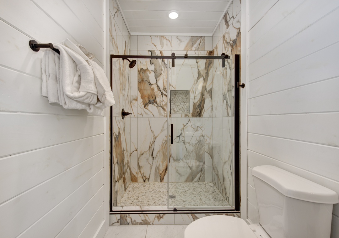 Step into your luxurious bathroom featuring a stunning marble shower with glass doors and plush towels awaiting your arrival.